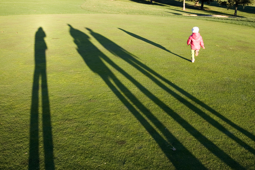 Tall shadows loom on golf course greens as a little girl runs for fun.